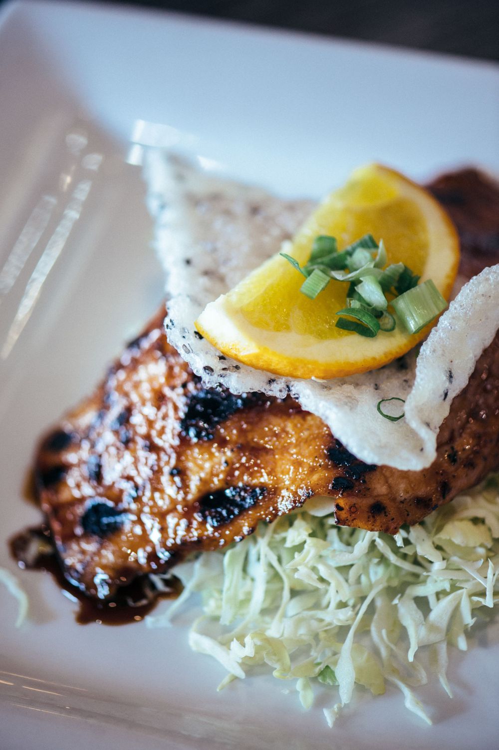 Grilled chicken served on shredded cabbage with lemon garnish and sauce on white plate.