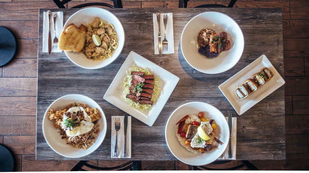 Overhead view of multiple place settings with various dishes on a dark wooden restaurant table.