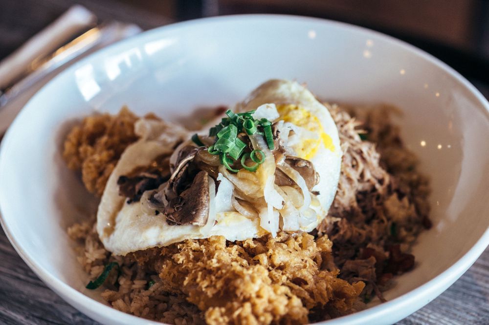 Fried rice topped with a sunny side up egg and fresh herbs served in a white bowl.