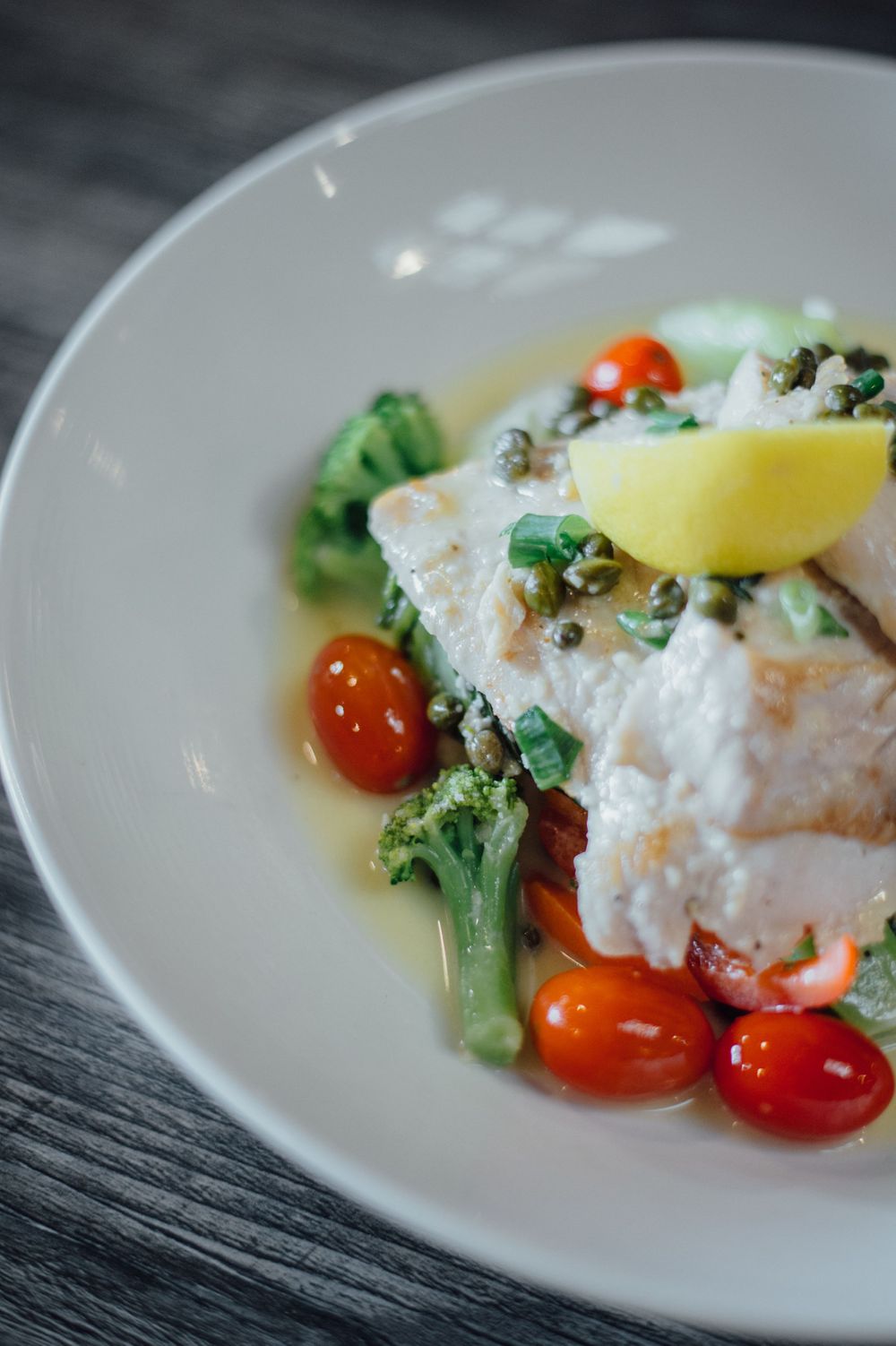 Pan-seared fish fillet with cherry tomatoes and broccoli in a light sauce on white plate.