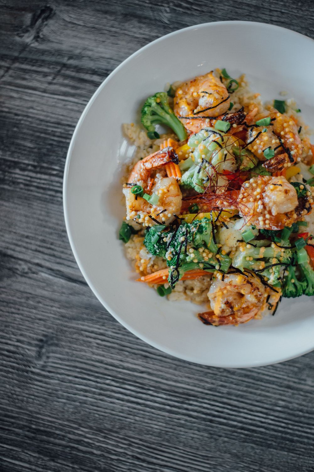Shrimp stir fry with vegetables and sesame seeds served on white plate.