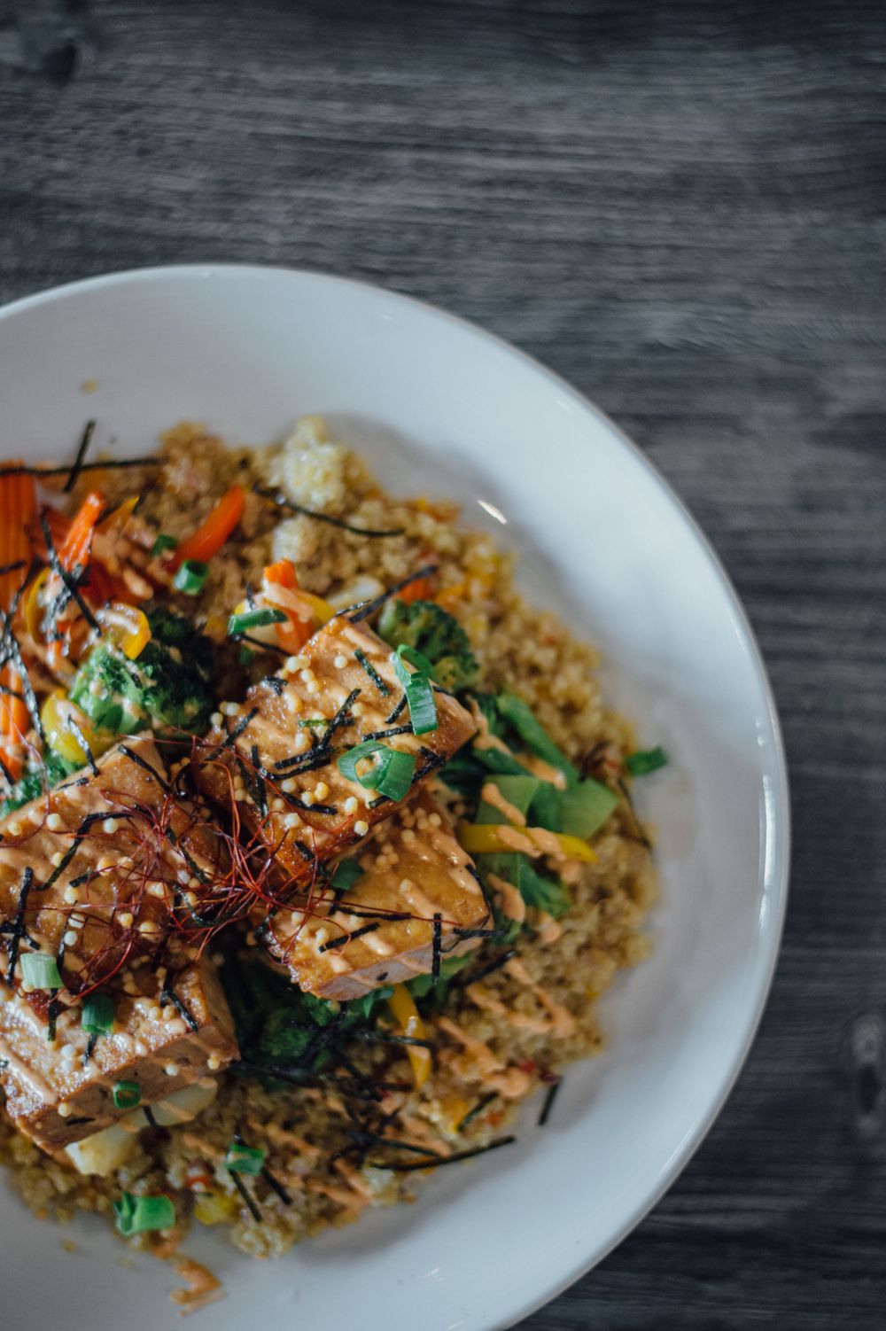 Asian rice bowl topped with vegetables and sesame seeds on white plate.