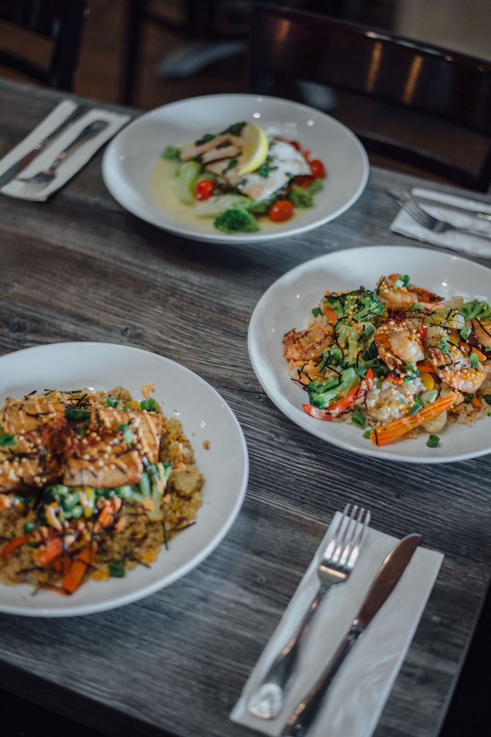 Multiple plates of colorful Asian fusion dishes arranged on rustic wooden table.