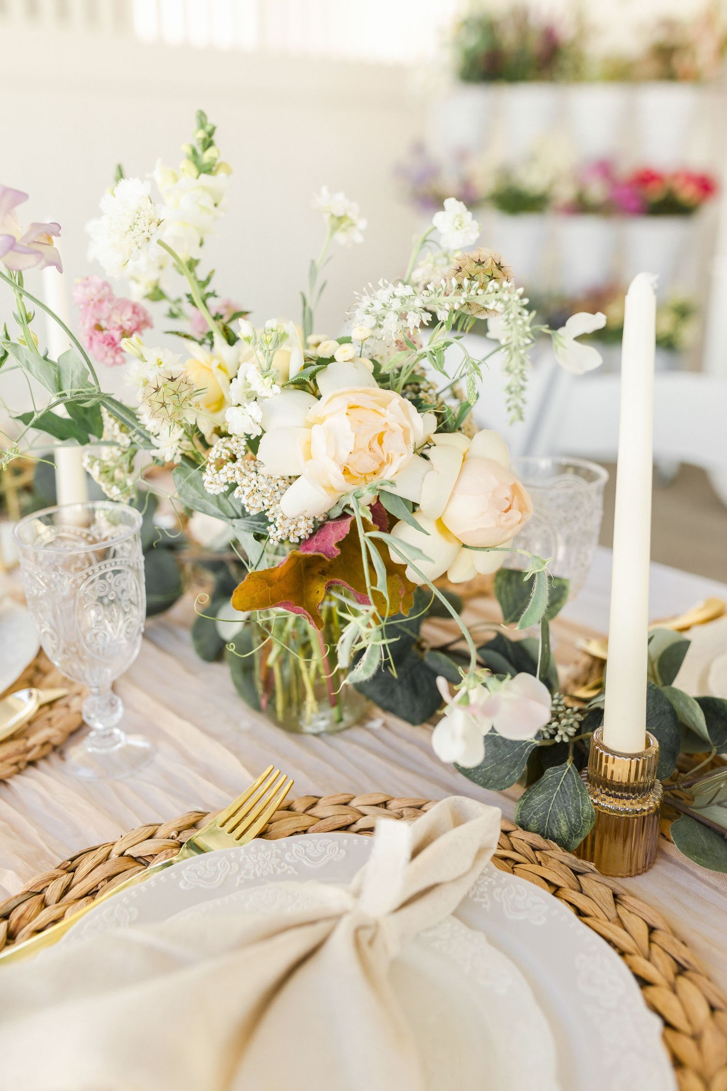 A delicate bouquet of daisies, pink roses, and wildflowers arranged in a glass vase against a bright white background by Chelsee Rawe Photo