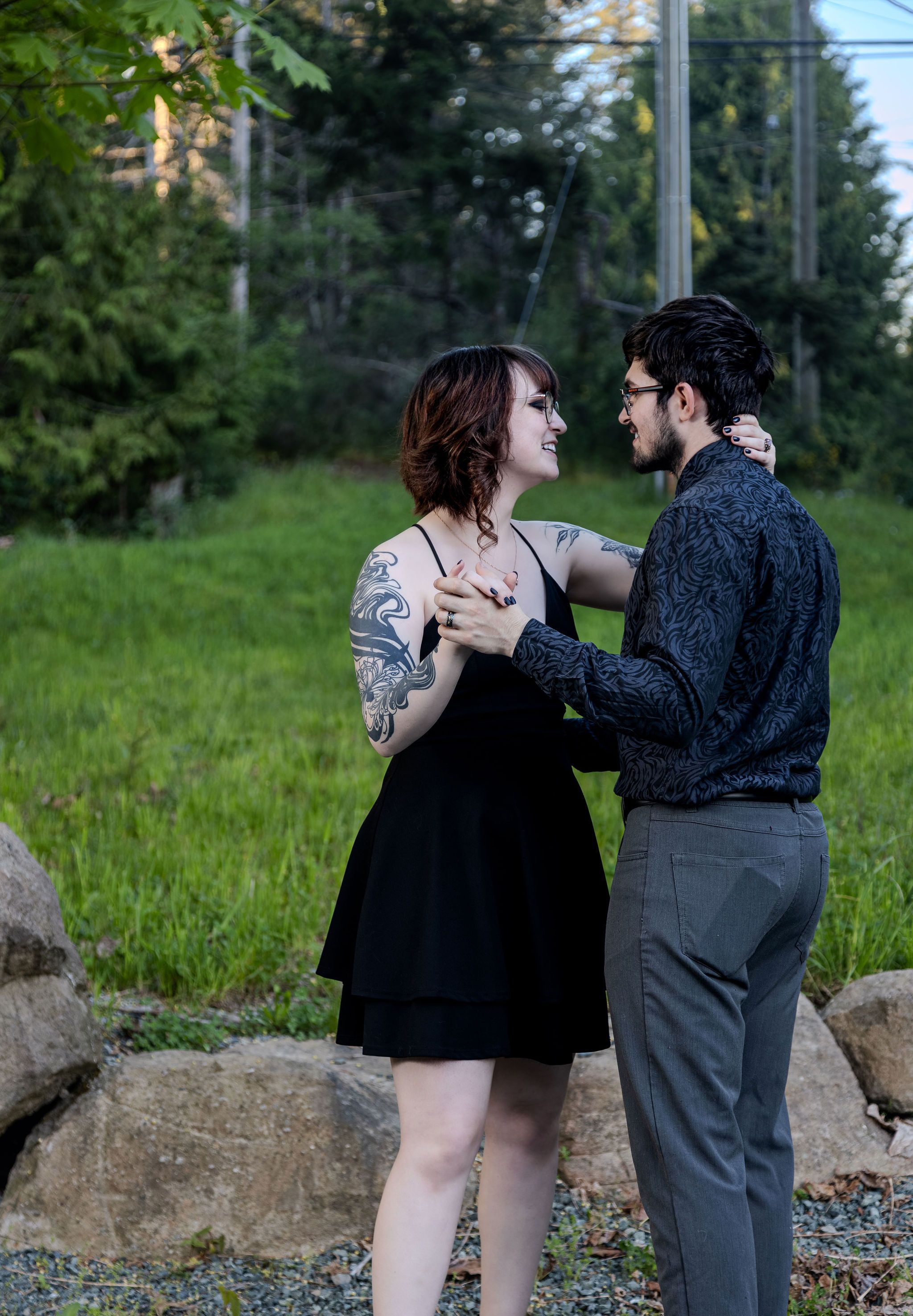 Happy couple dancing together outdoors, woman in black dress with sleeve tattoos, smiling.