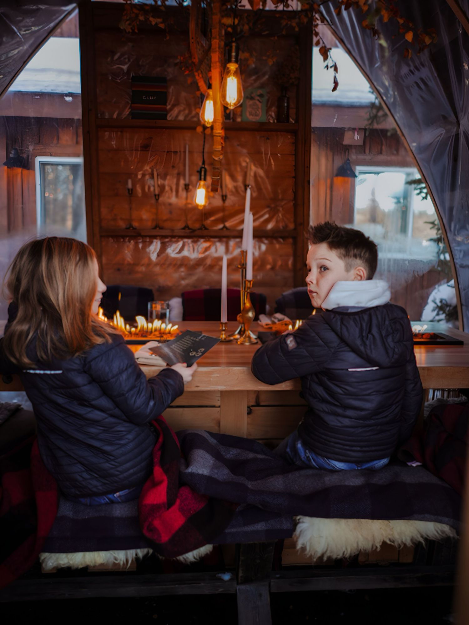 Two people dining at a cozy rustic restaurant booth with warm lighting and candles creating an intimate atmosphere.