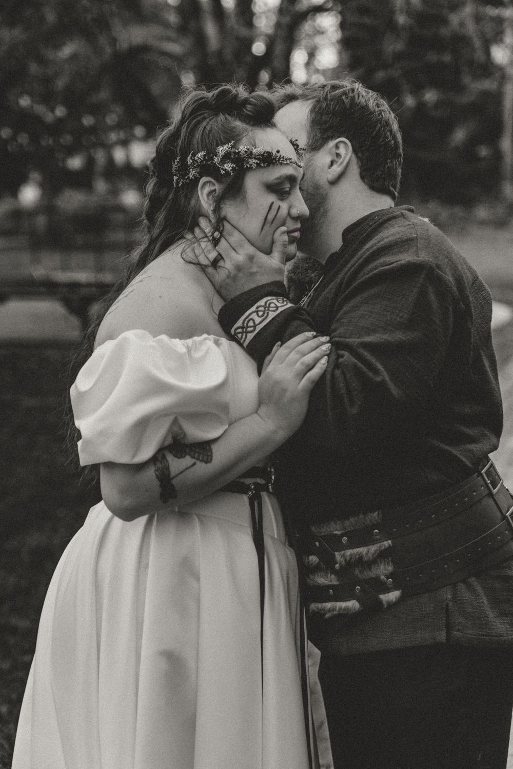 Black and white photo of a couple in medieval costumes sharing a romantic moment outdoors.