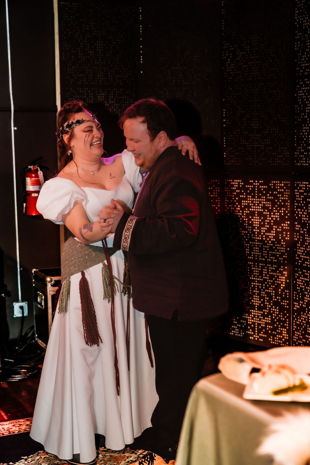 Bride and groom share a joyful dance at their wedding reception, smiling and embracing in elegant attire.