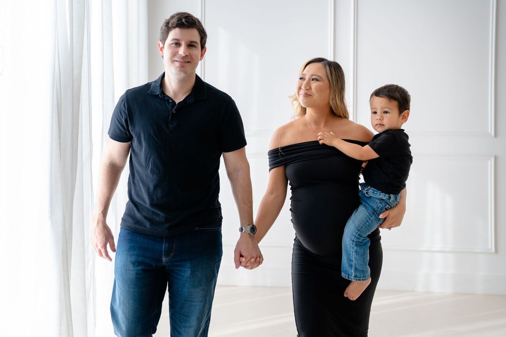 Family walks together holding hands in a bright white studio setting wearing casual clothing.