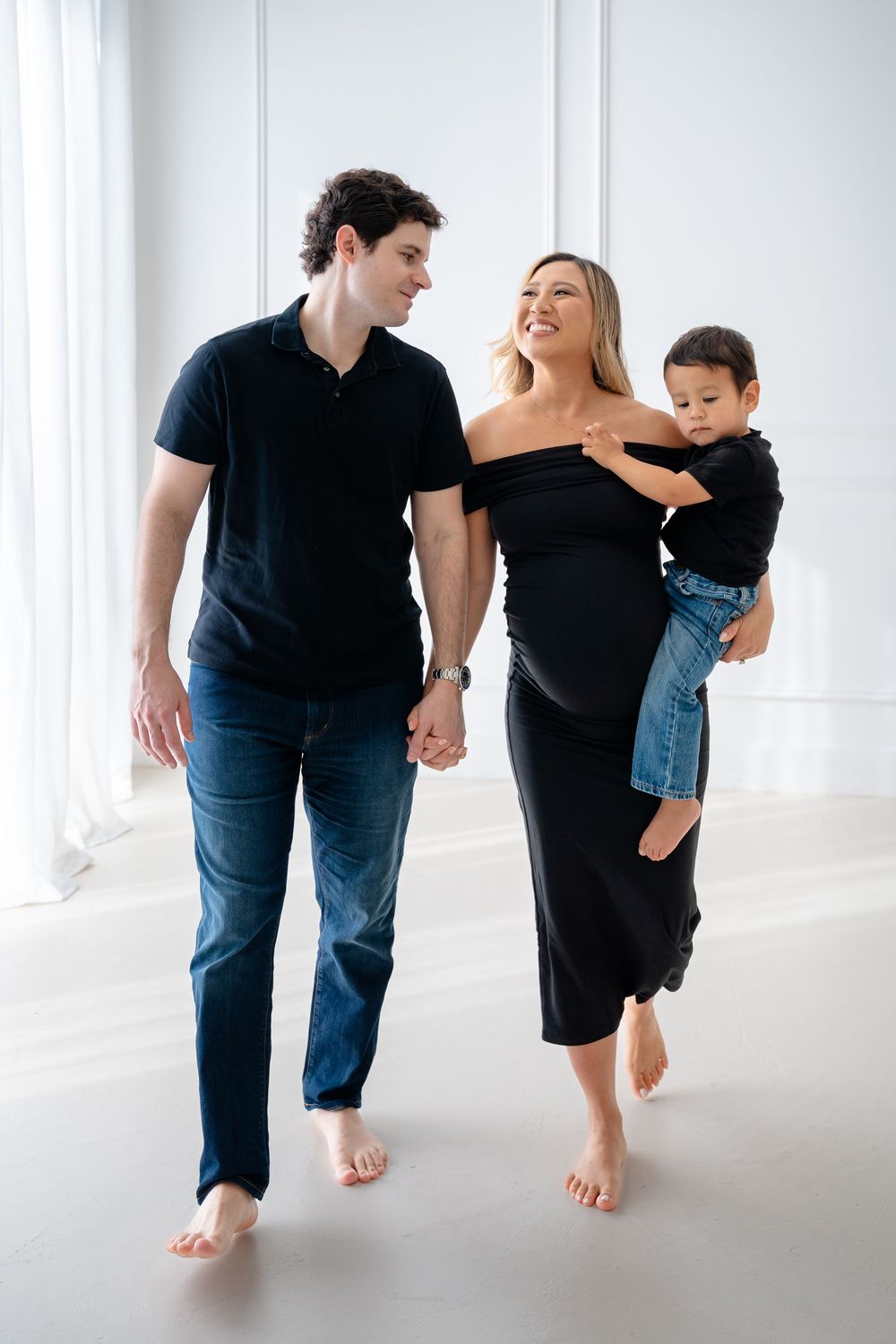 A family of three in black clothing dances together in a bright white studio space.