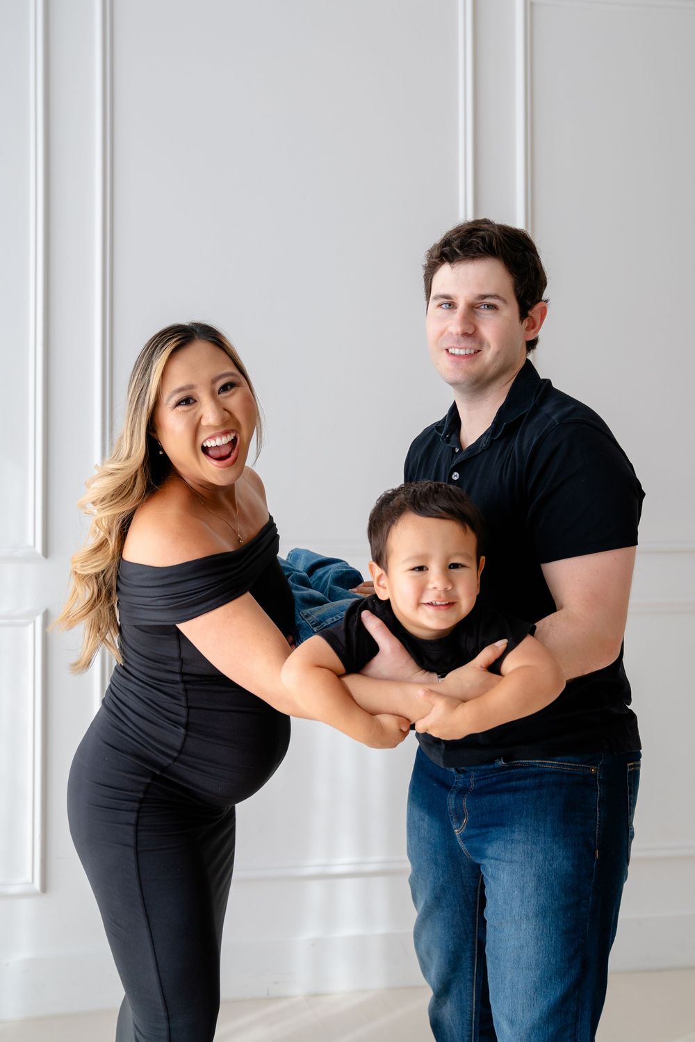 A family in matching black outfits playfully poses together against a white wall in a progressive series of fun movements.