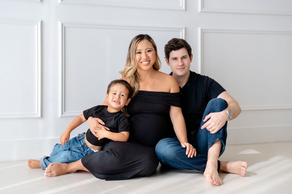 A family in casual clothing poses together on a white floor in a bright studio setting.