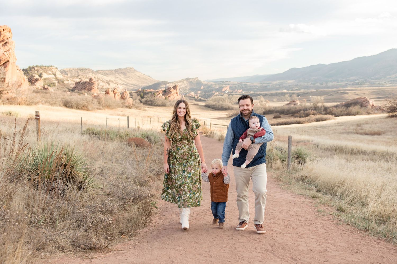 Group wearing coordinated outfits in earth tones and floral dresses pose together in a rustic field setting.