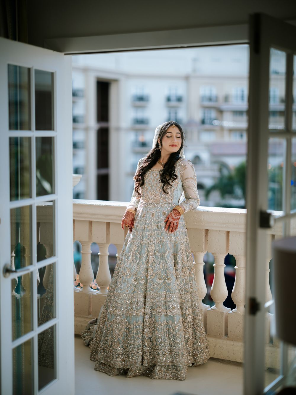 Elegant silver embroidered wedding lehenga shown in detail against an indoor balcony setting.