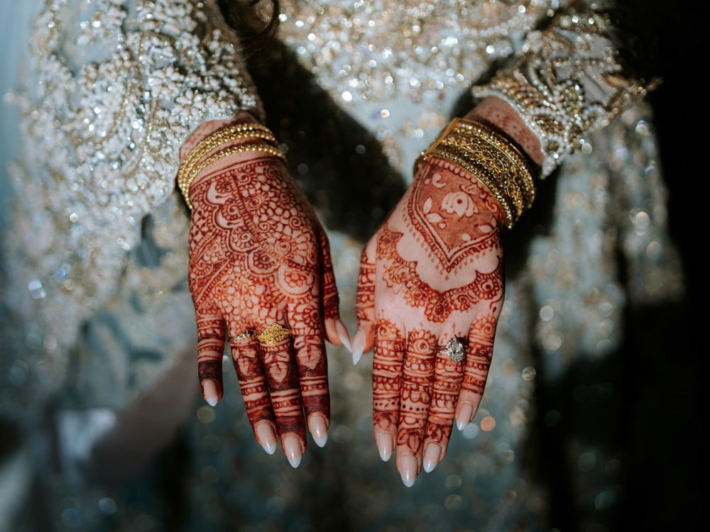 Intricate henna designs adorned on hands with sparkling lights in the background.