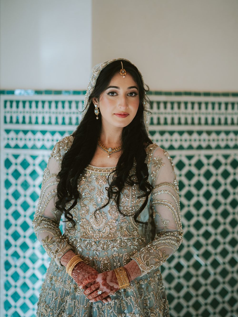 Traditional bridal attire featuring silver embellishments and turquoise geometric wall patterns.