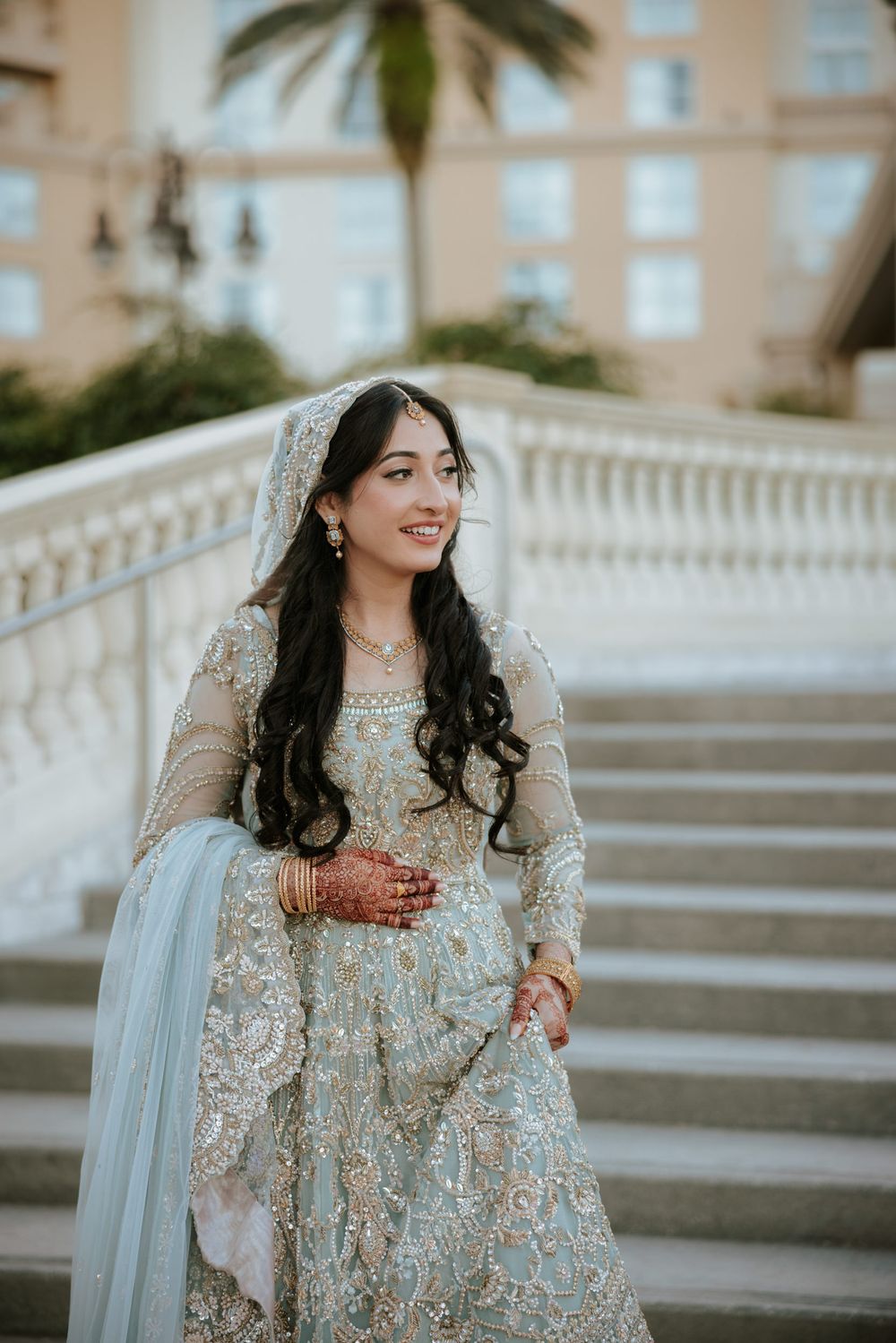 Elegant bridal portrait showcasing silver embroidered dress against a beige architectural backdrop.