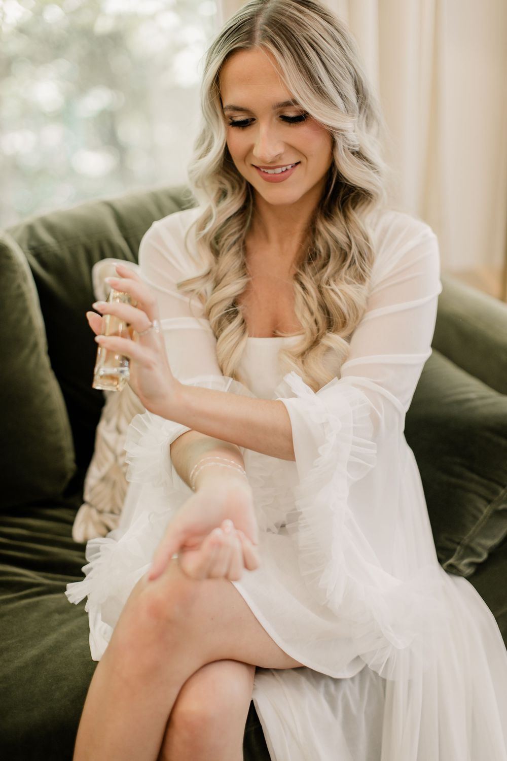 A person in a white silk robe sits on a green velvet couch during wedding preparations.
