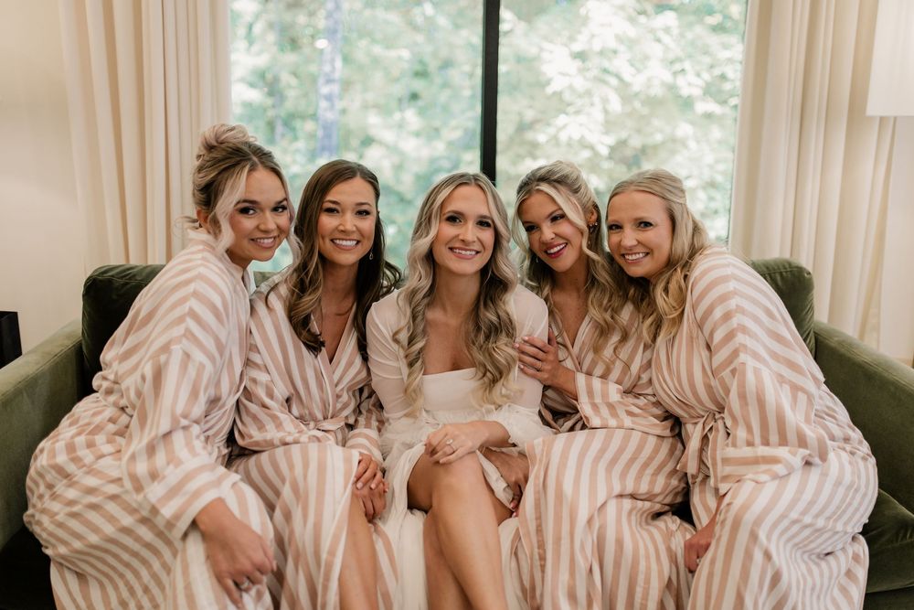 Wedding party in matching striped robes relaxing on a couch during preparations.