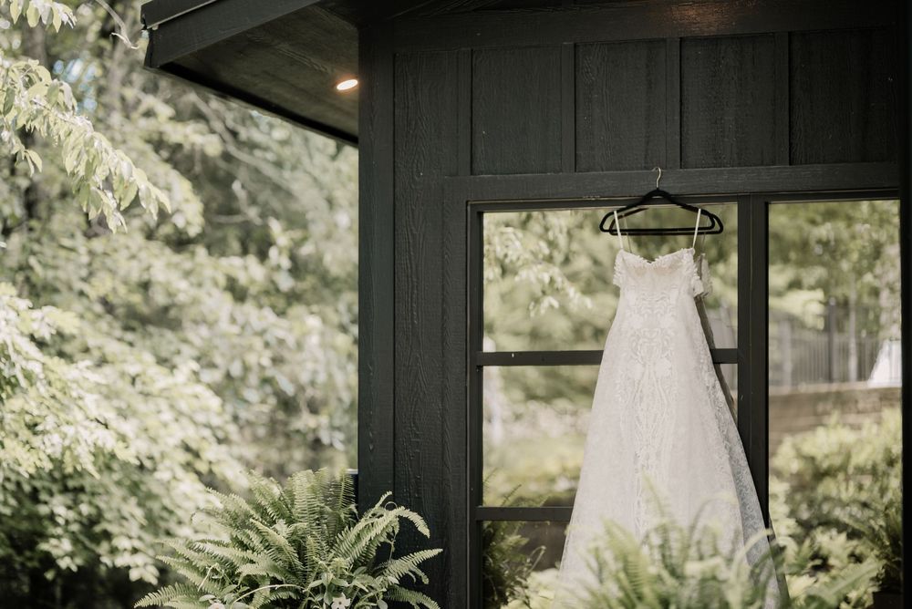 Wedding dress hanging in a dark room with natural light streaming through windows.