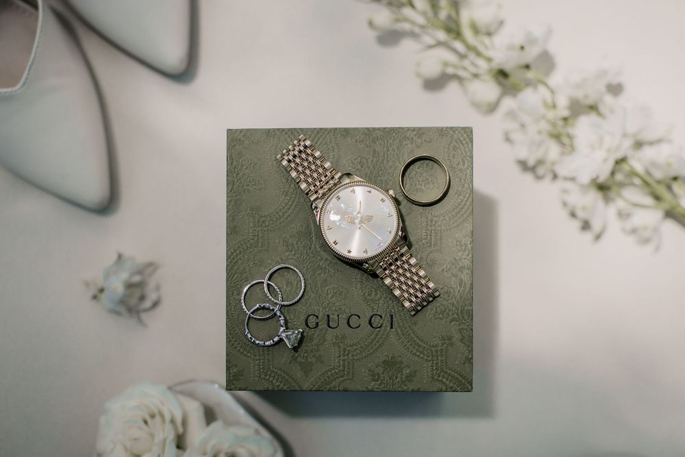Wedding accessories including rings, watch, and jewelry arranged on gray textured surfaces.