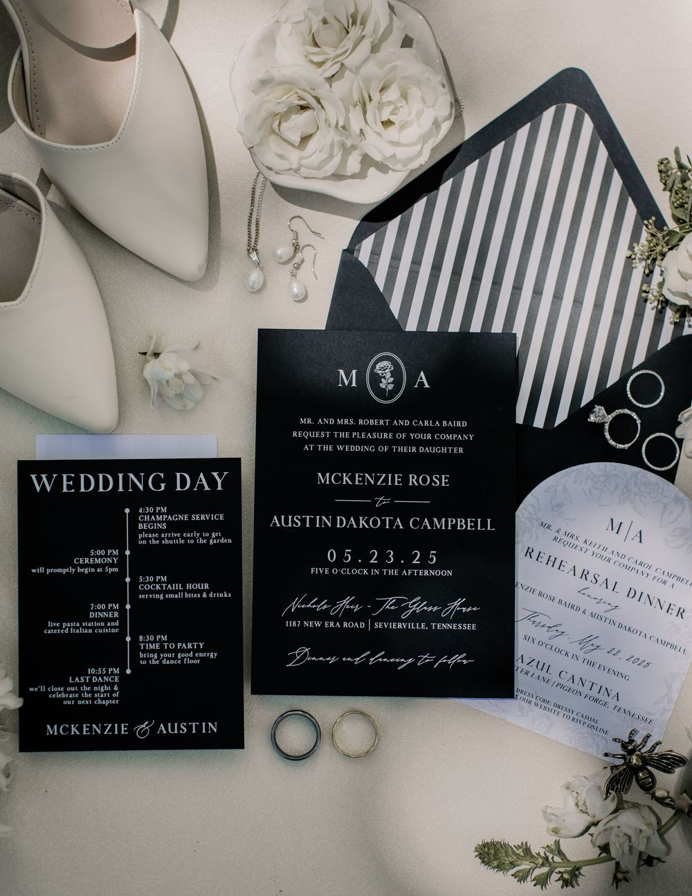 Elegant black and white wedding invitations and rings styled with white flowers and greenery.