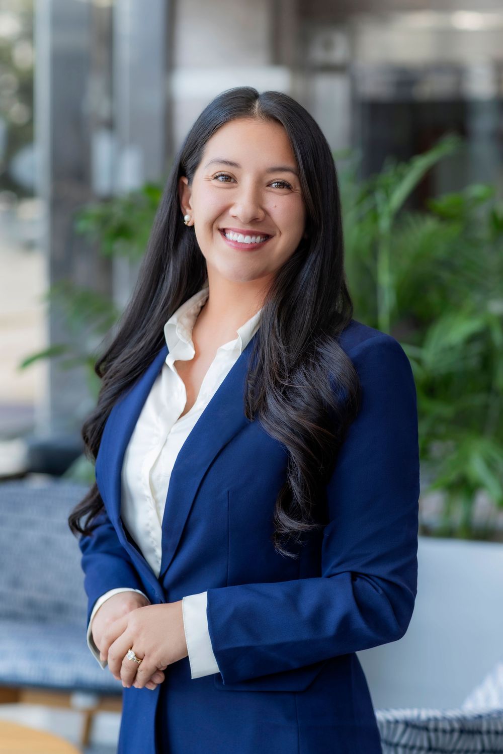 Professional headshots showing someone in a navy blazer and white shirt against a light background with greenery.