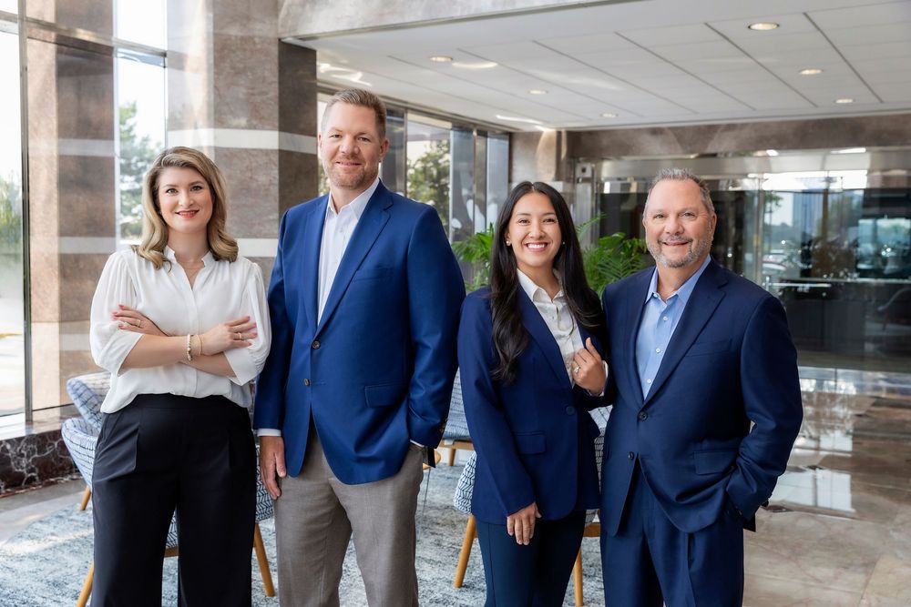 Professional business team members in navy suits and business attire pose together in modern office setting.