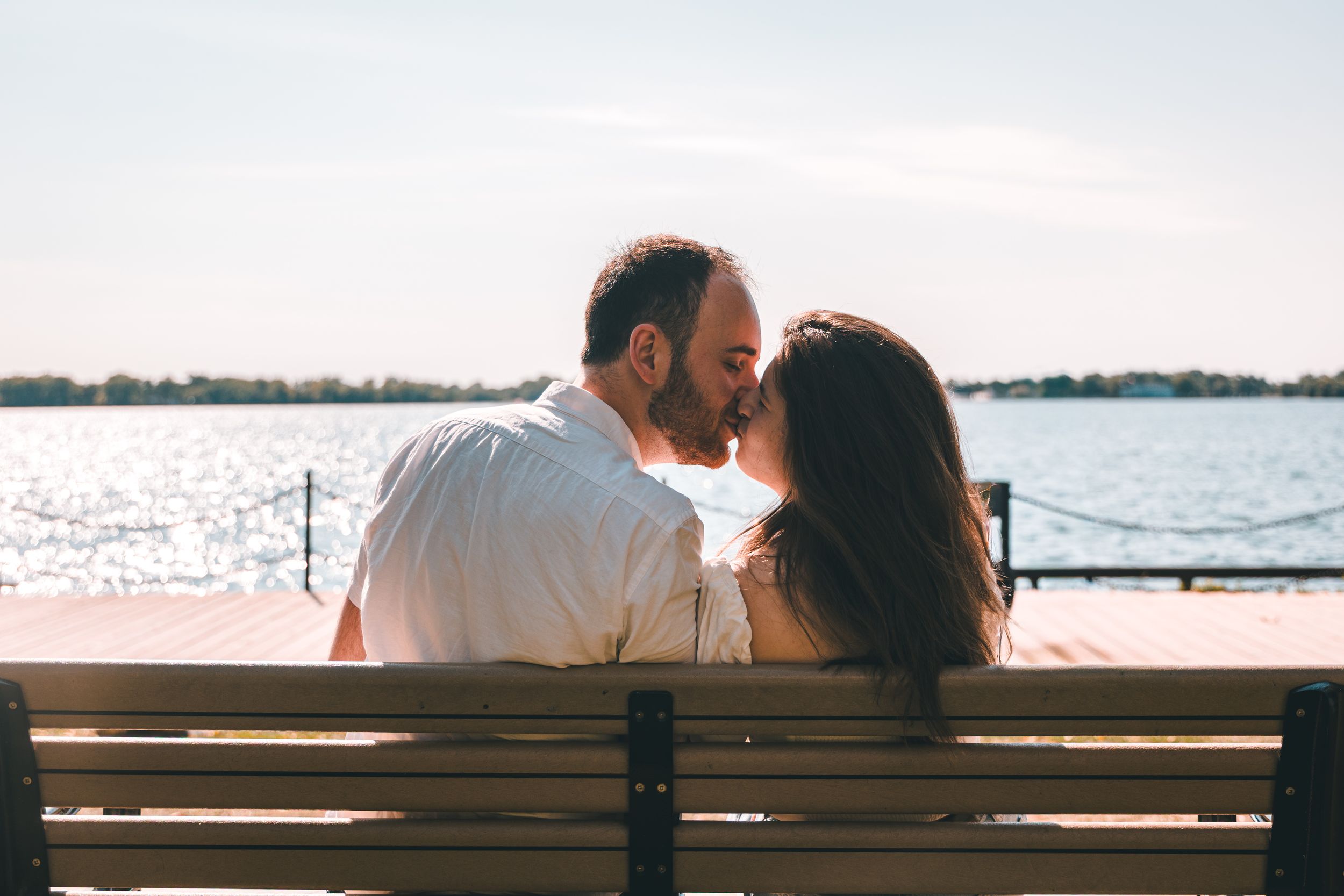 A couple sits together on a wooden bench overlooking a scenic waterfront view at sunset.