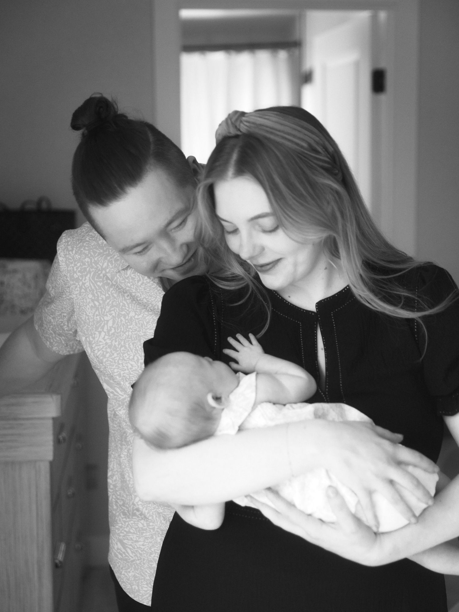 Black and white photo series showing a tender moment of someone holding and embracing a baby in a bright indoor space.