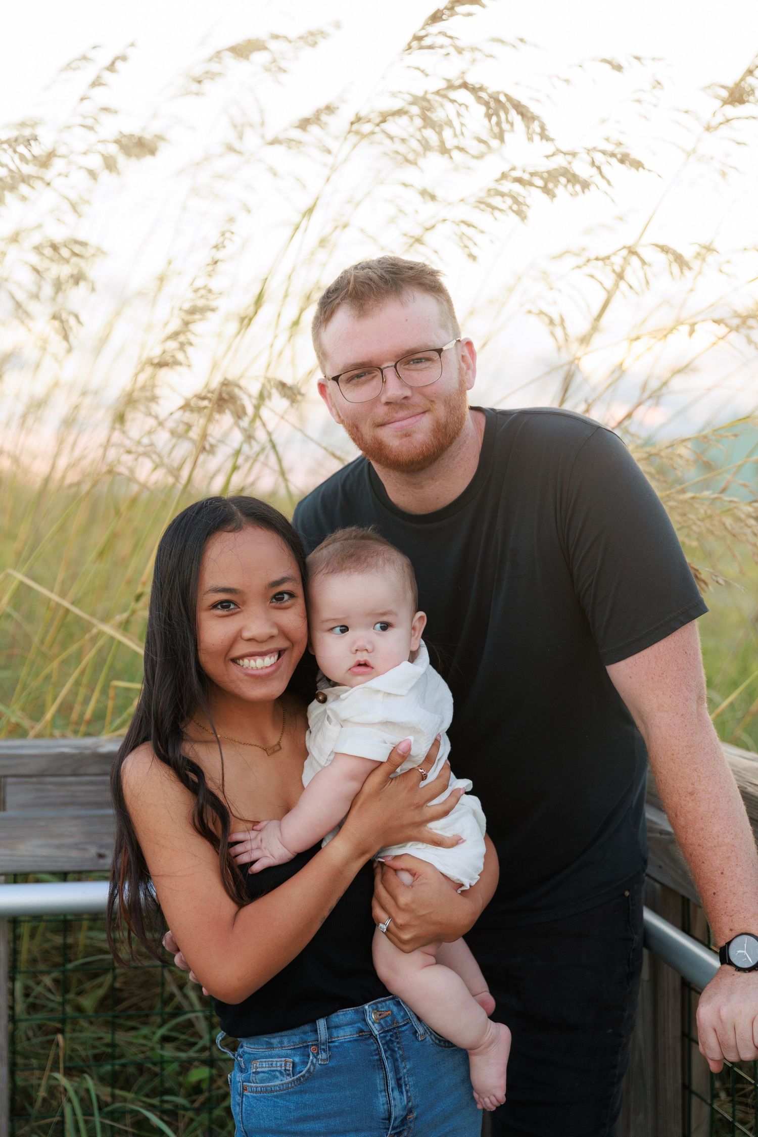 Family poses together in tall grass during sunset for outdoor photo session series.