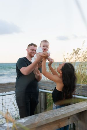 A family shares joyful moments together on a wooden deck by the beach at sunset.