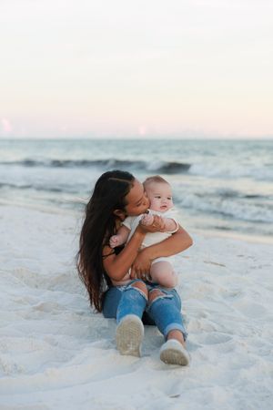 Parent and child share a tender moment while sitting together on a pristine white sandy beach at sunset.