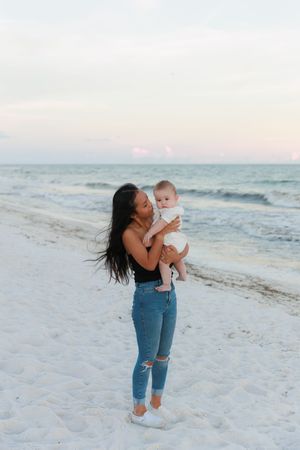 A mother and baby share joyful moments together while playing on a white sandy beach at sunset.