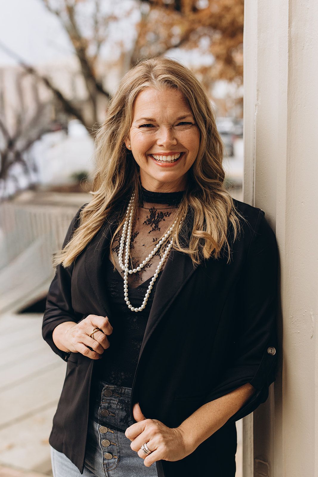 Professional lifestyle portrait series showing someone in a black blazer and pearl necklaces against a light outdoor background.