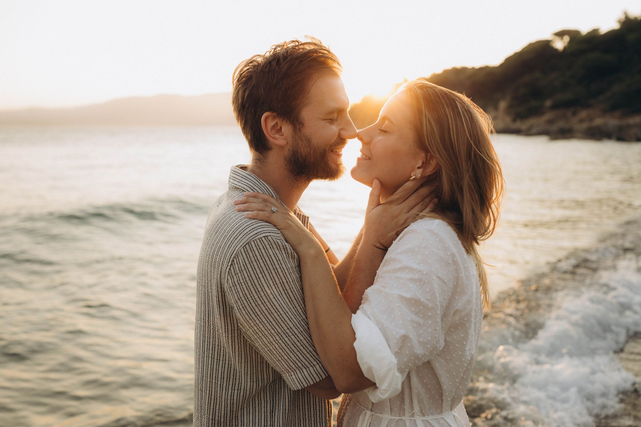 A romantic couple shares tender moments on a beach at sunset with golden light illuminating their silhouettes.