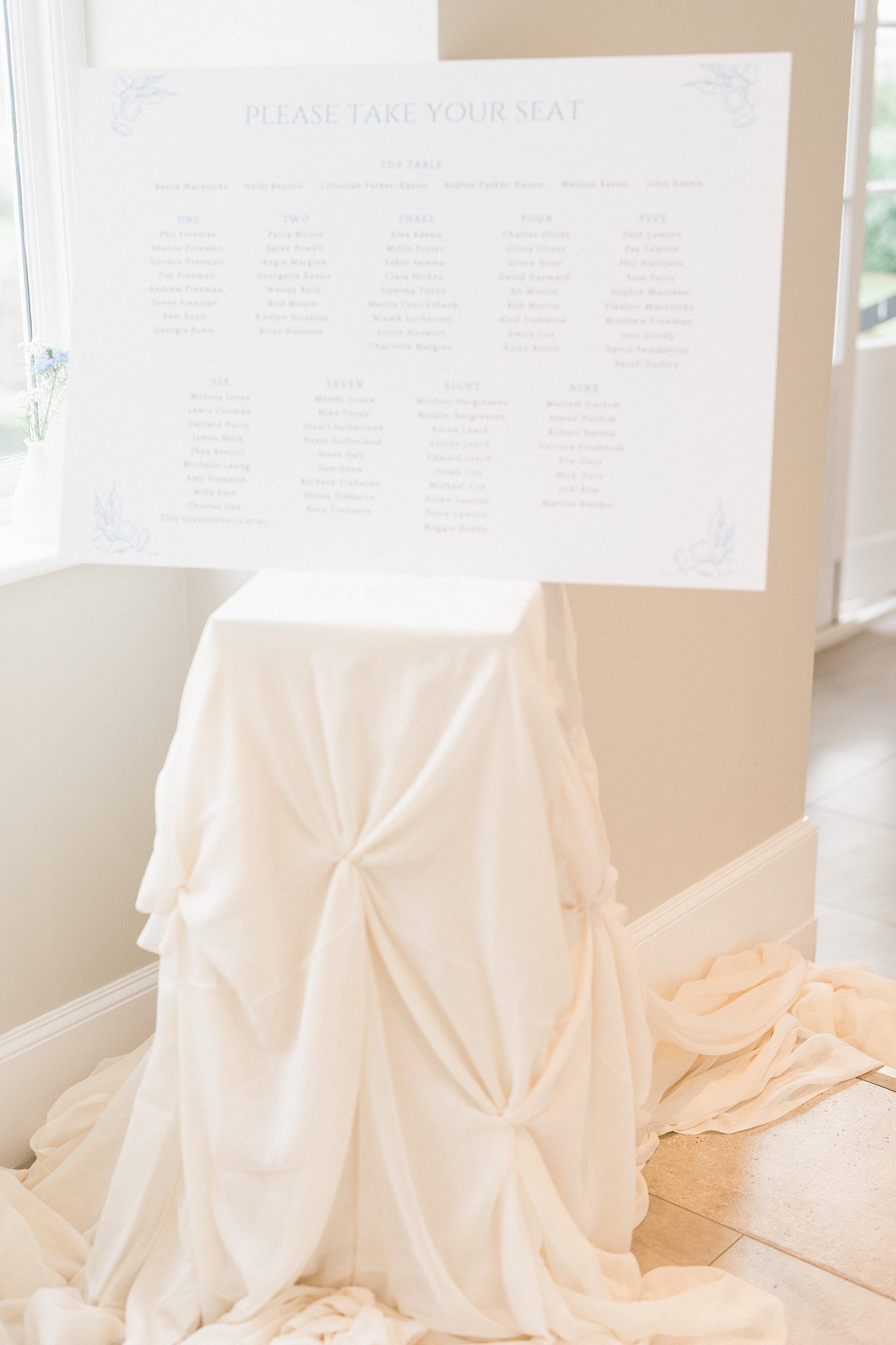 Elegant white fabric seating chart display with delicate draping creates a romantic wedding reception focal point.