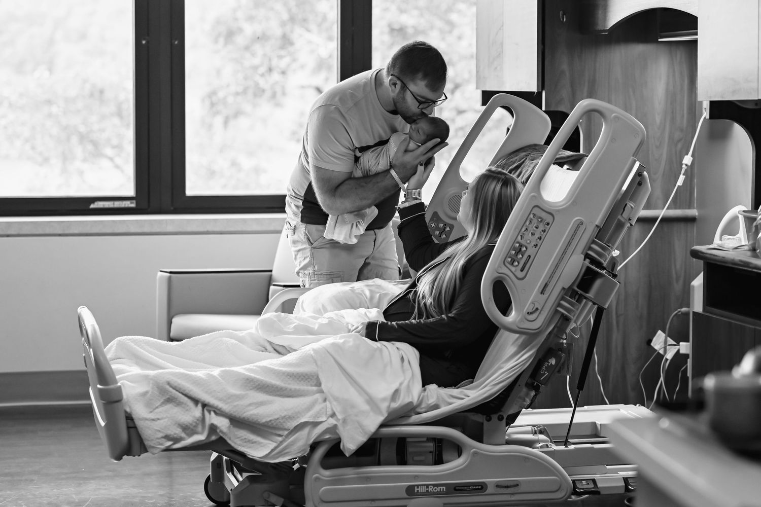 New dad with newborn baby and wife in hospital room.