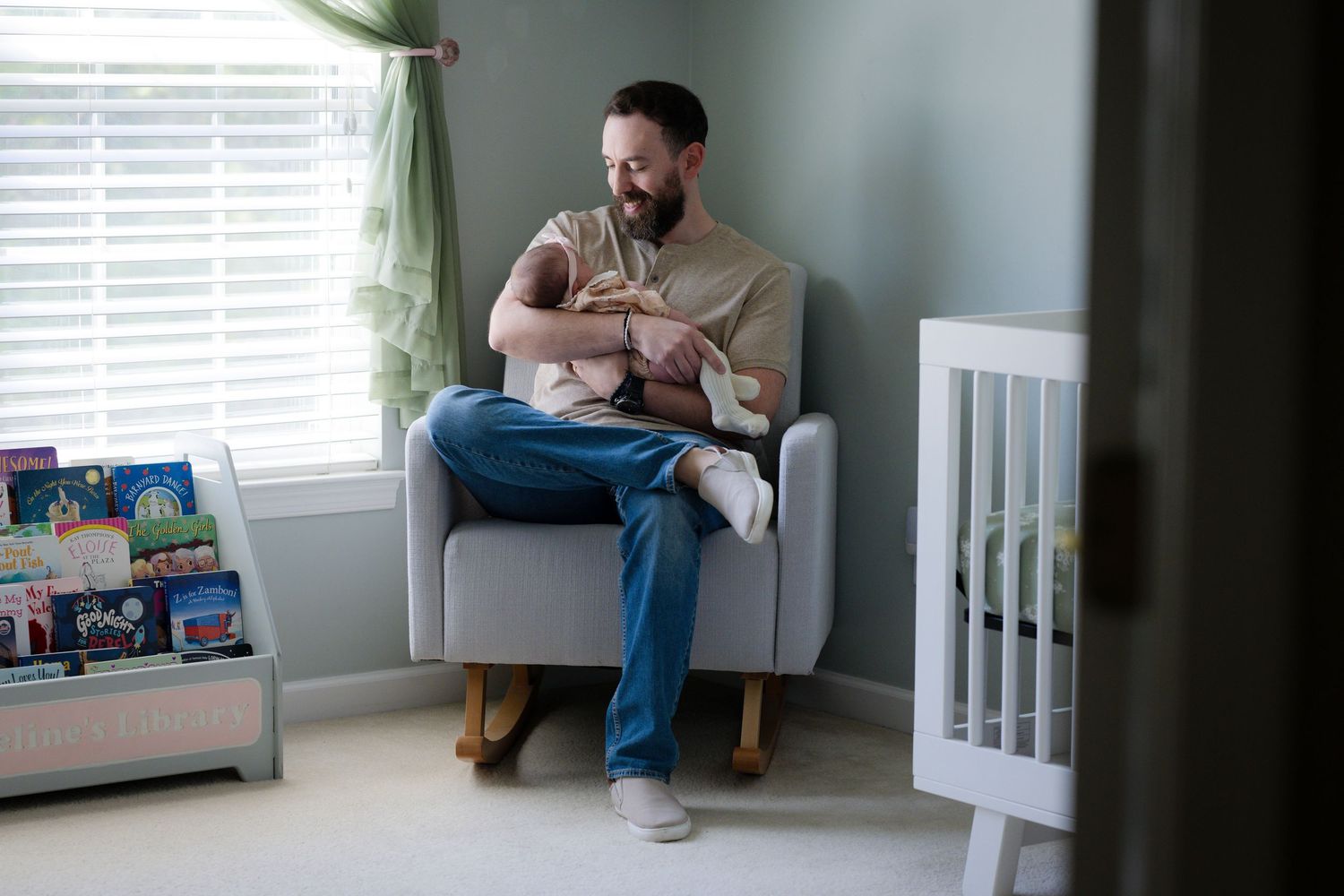 Parent sitting in nursery armchair holding and feeding newborn baby.