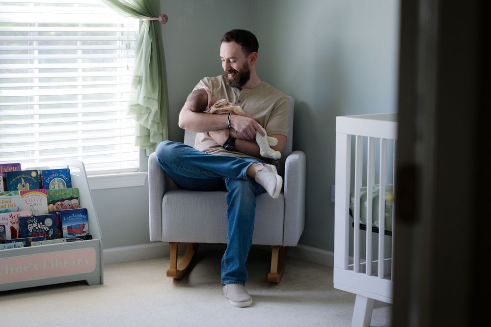 Parent sitting in nursery armchair holding and feeding newborn baby.