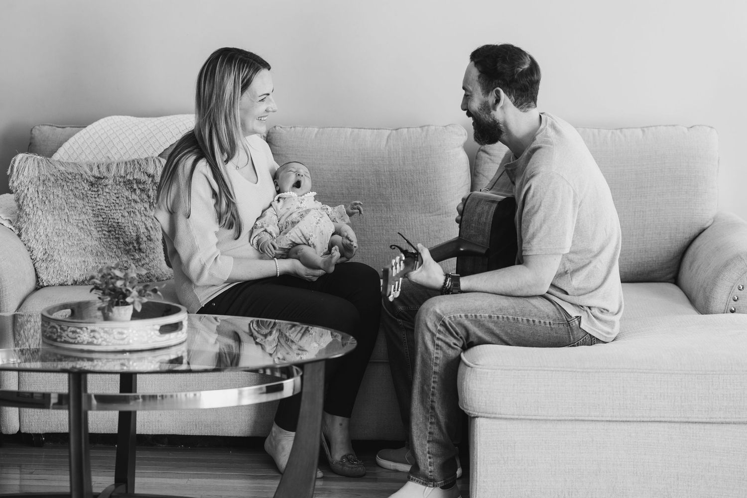 Parents sitting on couch having conversation while holding newborn baby.
