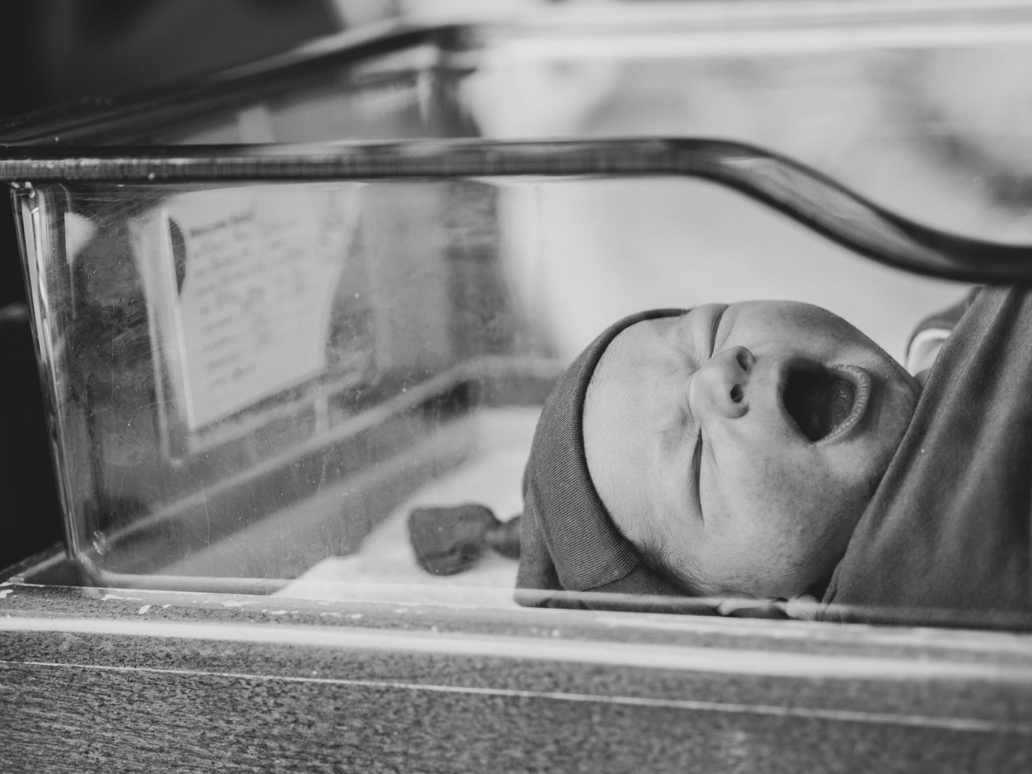 Black and white image of newborn baby in hospital bassinet.