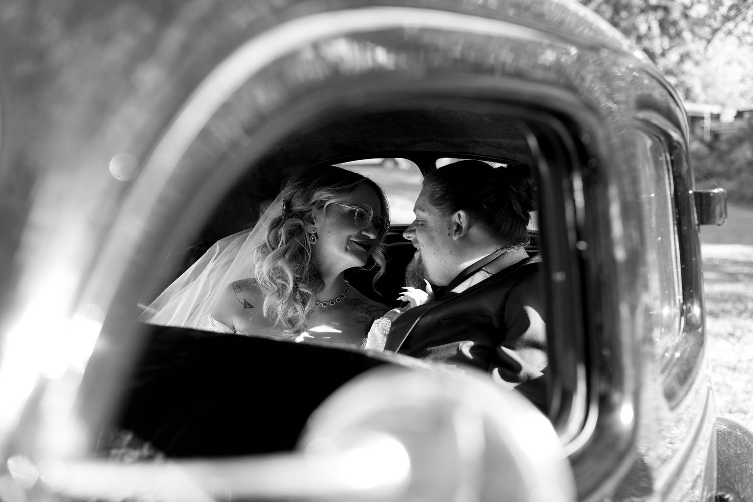 A bride and groom share a kiss in the backseat of their vintage car after their wedding ceremony.
