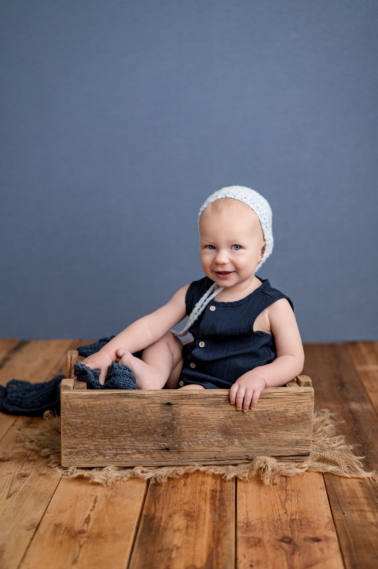 Small child in pink dress and boots sits on wooden chair against light colored wall with floral hair accessories.