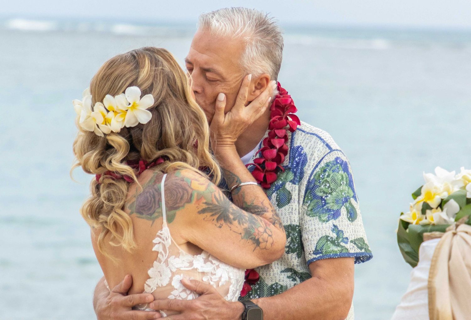 Romantic beach wedding couple sharing intimate moments by the ocean with tropical flowers and Hawaiian attire.