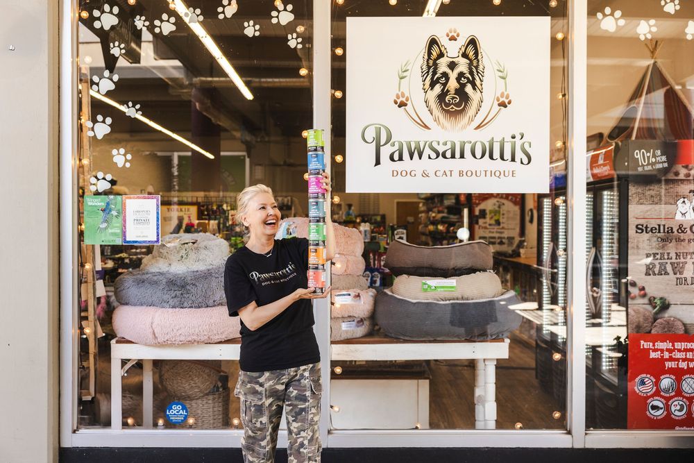 A pet grooming salon storefront with paw print decorations and signage displaying 'Pawsativity' in the window.
