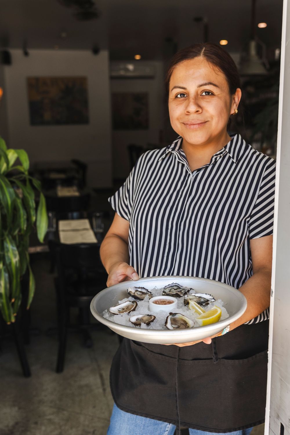 A restaurant server in a striped shirt holds a plate of fresh oysters with lemon and sauce.