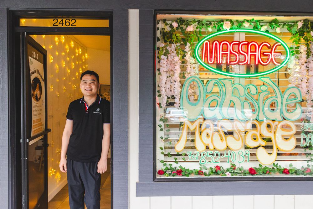A row of illuminated massage parlor storefront signs glowing in neon colors at night.