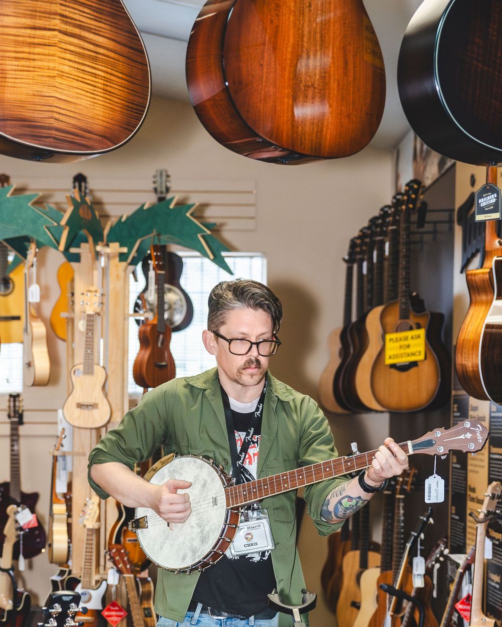 Musical instruments including guitars and banjos hang on display in a retail store with warm lighting.