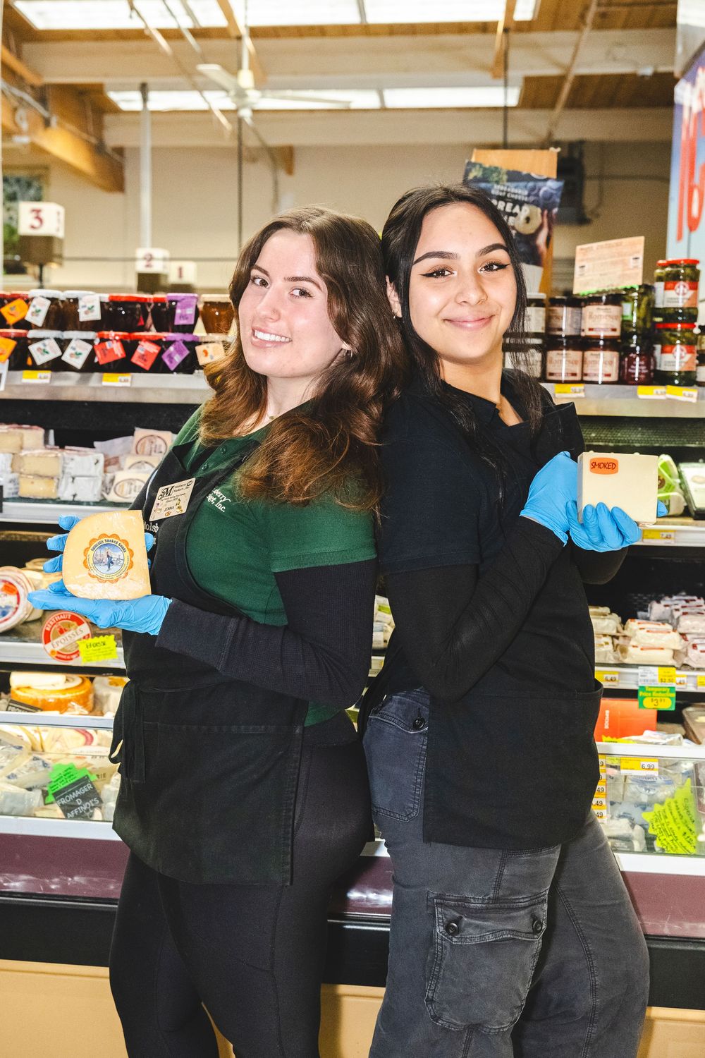 Store employees in green and black uniforms pose together while stocking shelves at a grocery store.